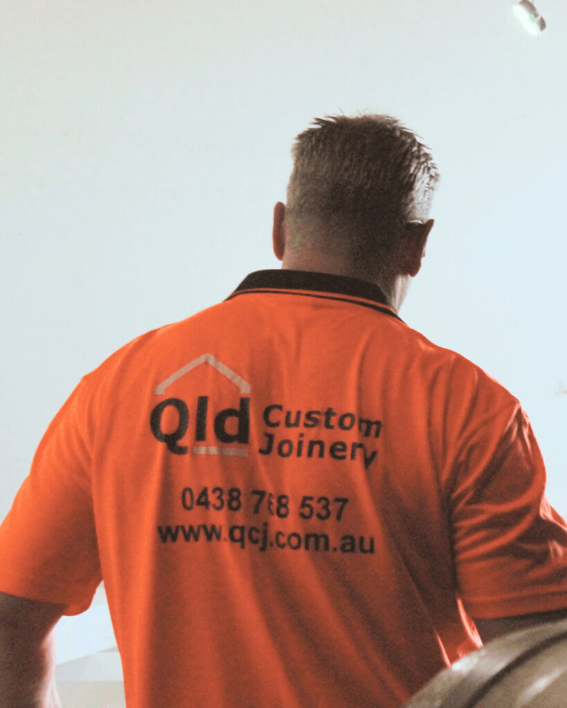 Back view of Jason wearing Qld Custom Joinery shirt displaying company details.